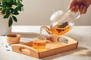 Tee wird aus einer Kanne in eine Tasse ausgeschenkt